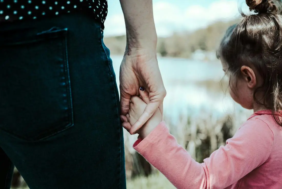 A parent holding a young child's hand